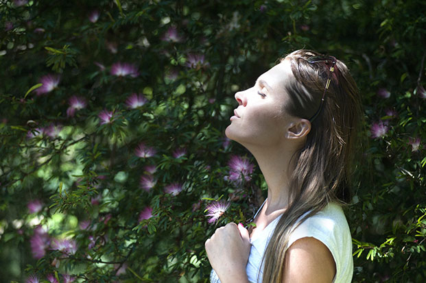 A woman in a white shirt breathes in the clean air beside lush, green foliage