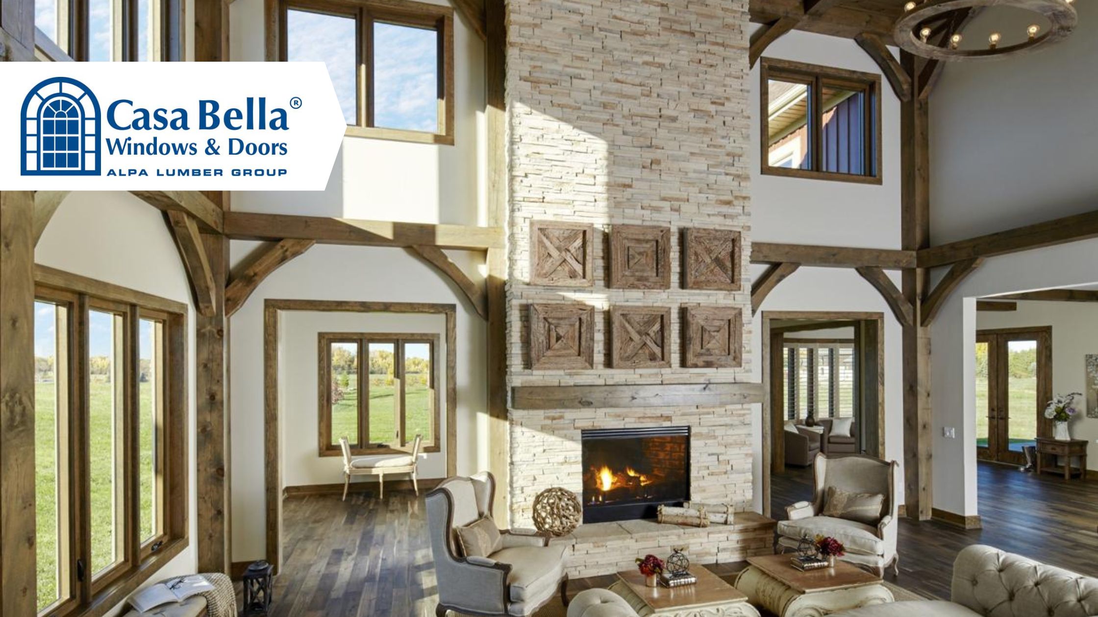 Rustic luxury home interior featuring large custom Casa Bella windows, exposed wood beams, stone fireplace, and abundant natural light